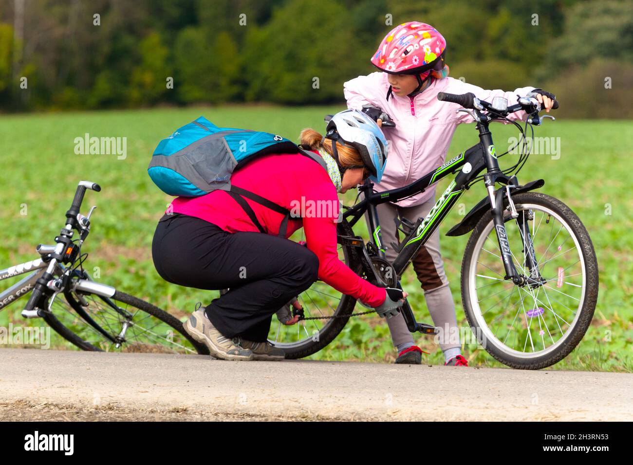 Mujer ayudando a ponerse una cadena caída, reparando bicicleta, un niño en casco, bicicleta Foto de stock