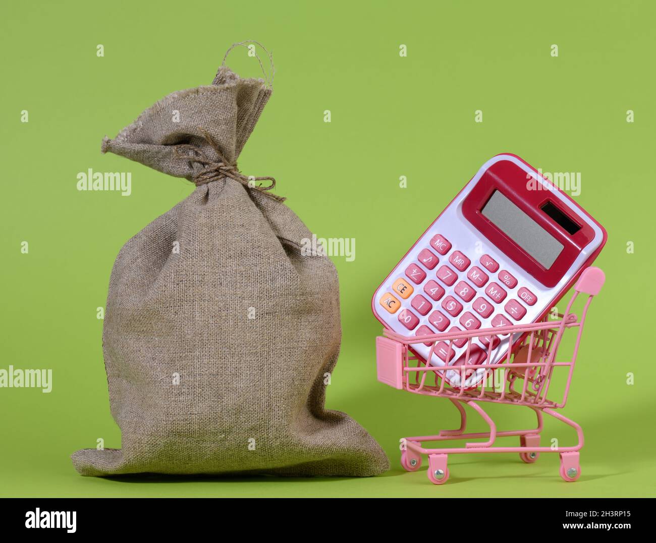 Bolsa de lona completa, calculadora de plástico rosa en un carrito de compras de metal en miniatura sobre un fondo verde Foto de stock