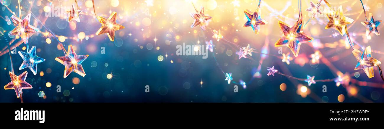 Estrellas de Navidad con luces doradas colgando de fondo azul - Cadena con Bokeh abstracto desfocado Foto de stock