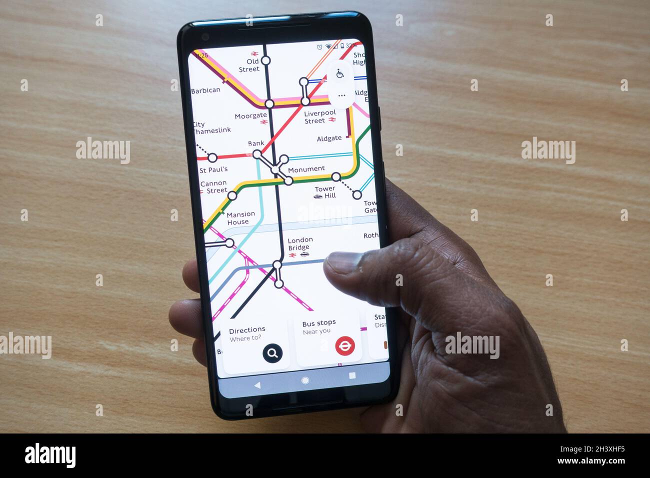 Hombre adulto sosteniendo un smartphone con un mapa de London Tube en la pantalla comprobando las conexiones de la estación Foto de stock