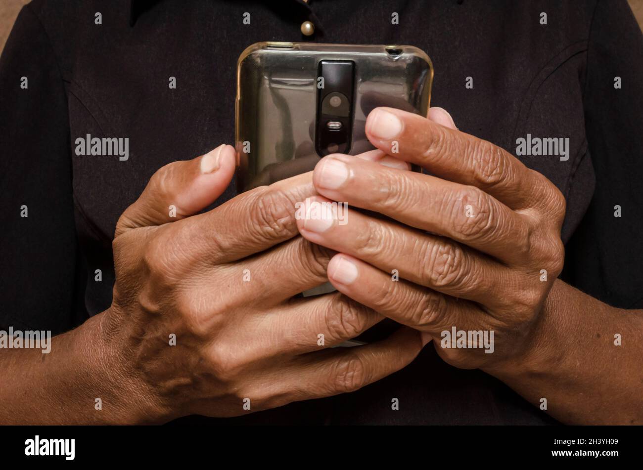 Manos de una mujer jamaicana que tiene más de cincuenta y cinco años sostiene un teléfono móvil Foto de stock
