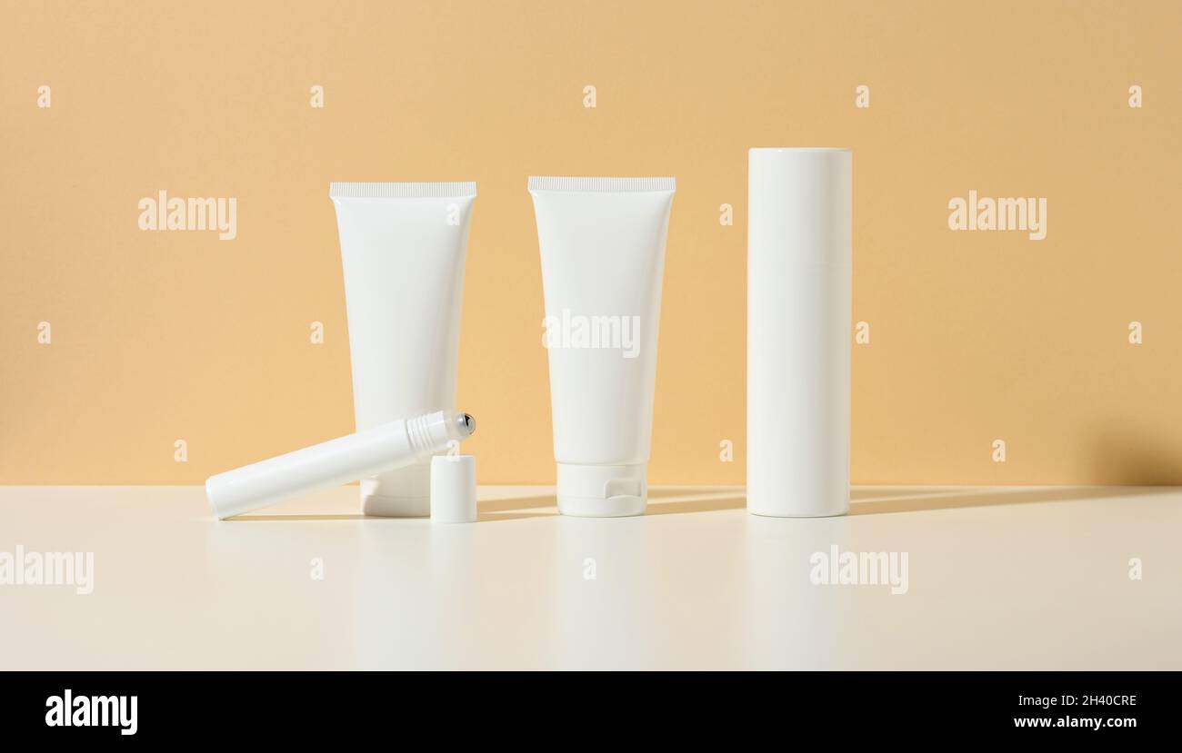 Tubo de plástico blanco vacío, rodillo delgado, botella sobre fondo beige. Productos cosméticos para la marca de gel, crema, loción, champú. Foto de stock