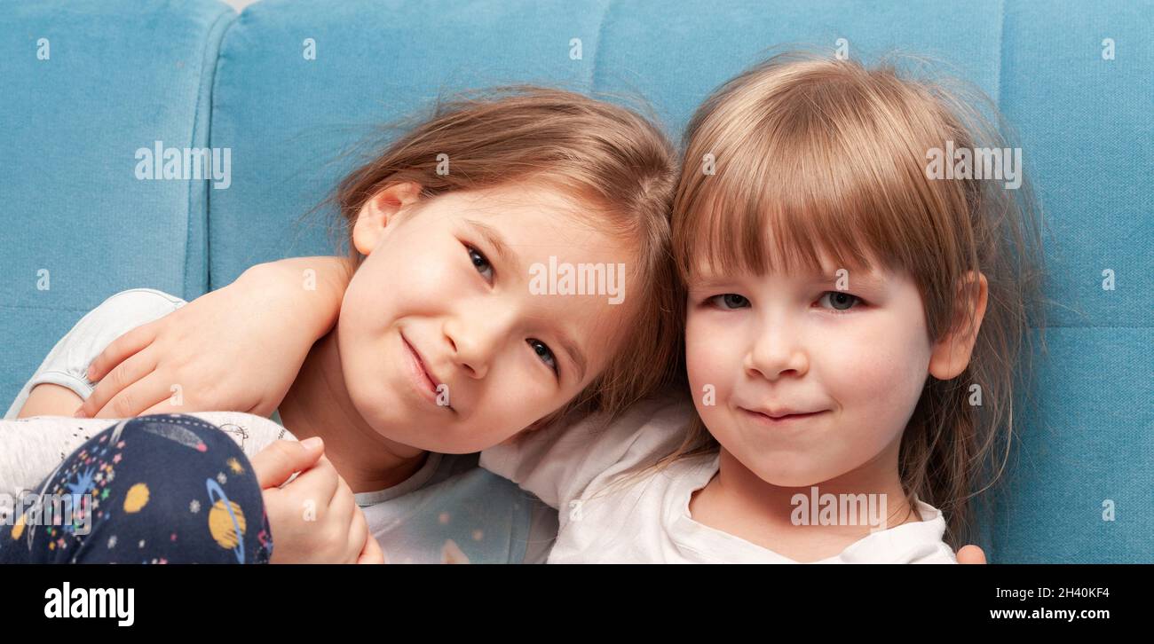 Dos jóvenes alegres niñas en edad de escuela primaria sonriendo, hermanas, hermanos abrazando, sentados juntos en un sofá, retrato, cara de primer plano. Familia Foto de stock