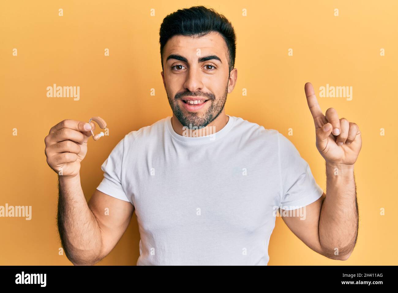 Joven hispano sosteniendo el auricular para sordera sonriendo con una idea  o pregunta señalando el dedo con la cara feliz, número uno Fotografía de  stock - Alamy