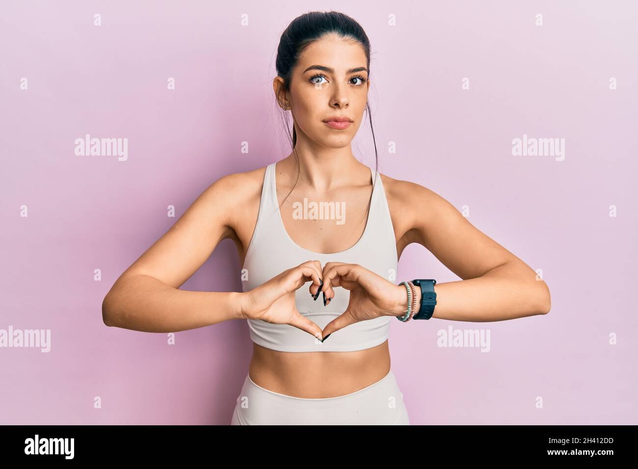 Mujer joven hispana con ropa deportiva haciendo símbolo del corazón con las  manos relajadas con expresión seria en la cara. Simple y natural mirando al  camer Fotografía de stock - Alamy