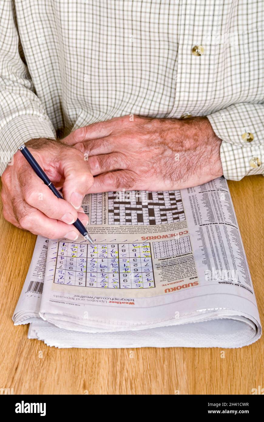 Primer plano vertical de un caballero mayor haciendo el rompecabezas 'Sudoku' en su periódico diario. Foto de stock