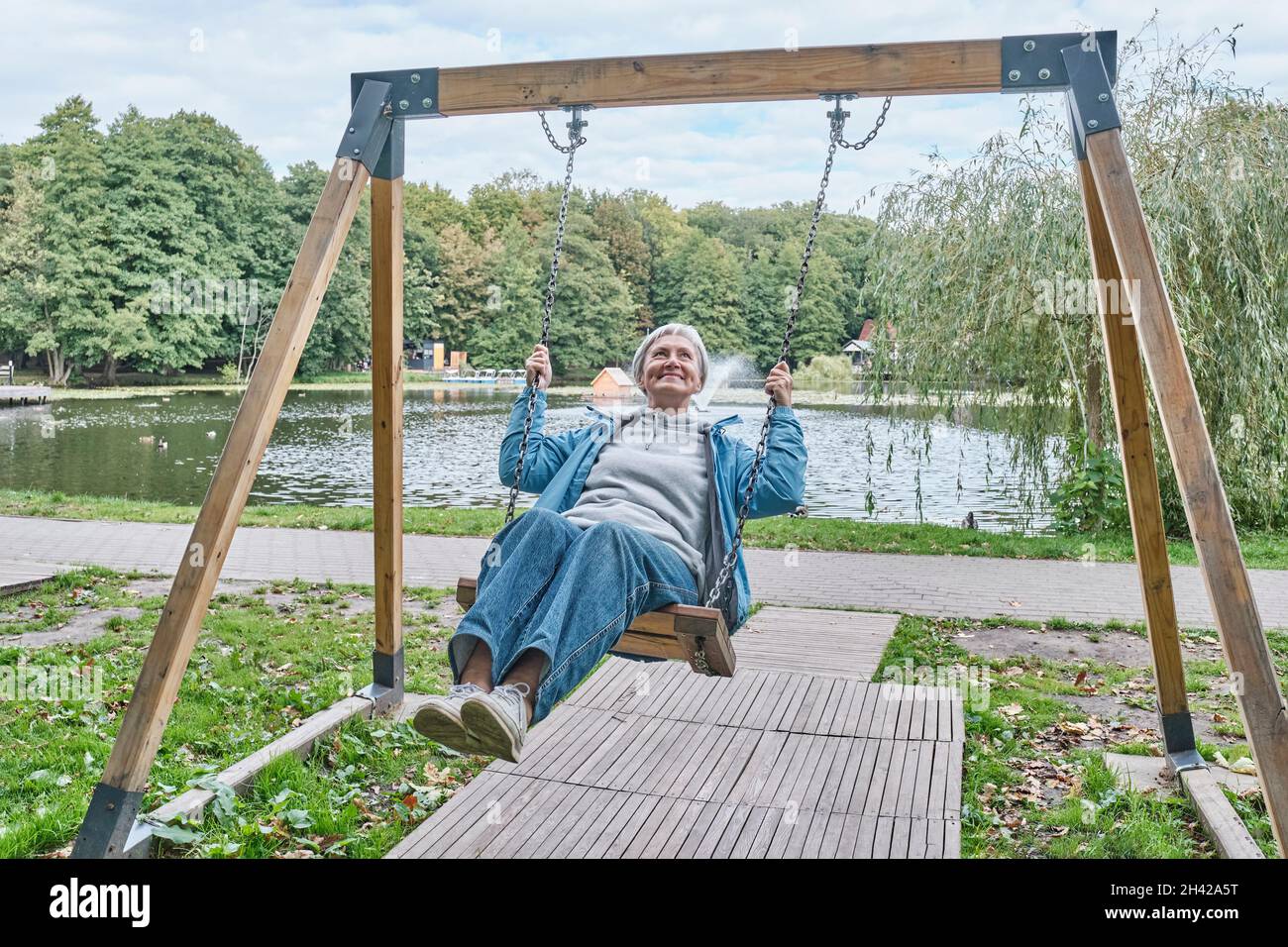 Feliz mujer mayor caucásica con el pelo gris corto que se balancea en el  columpio de la cadena en el parque Fotografía de stock - Alamy