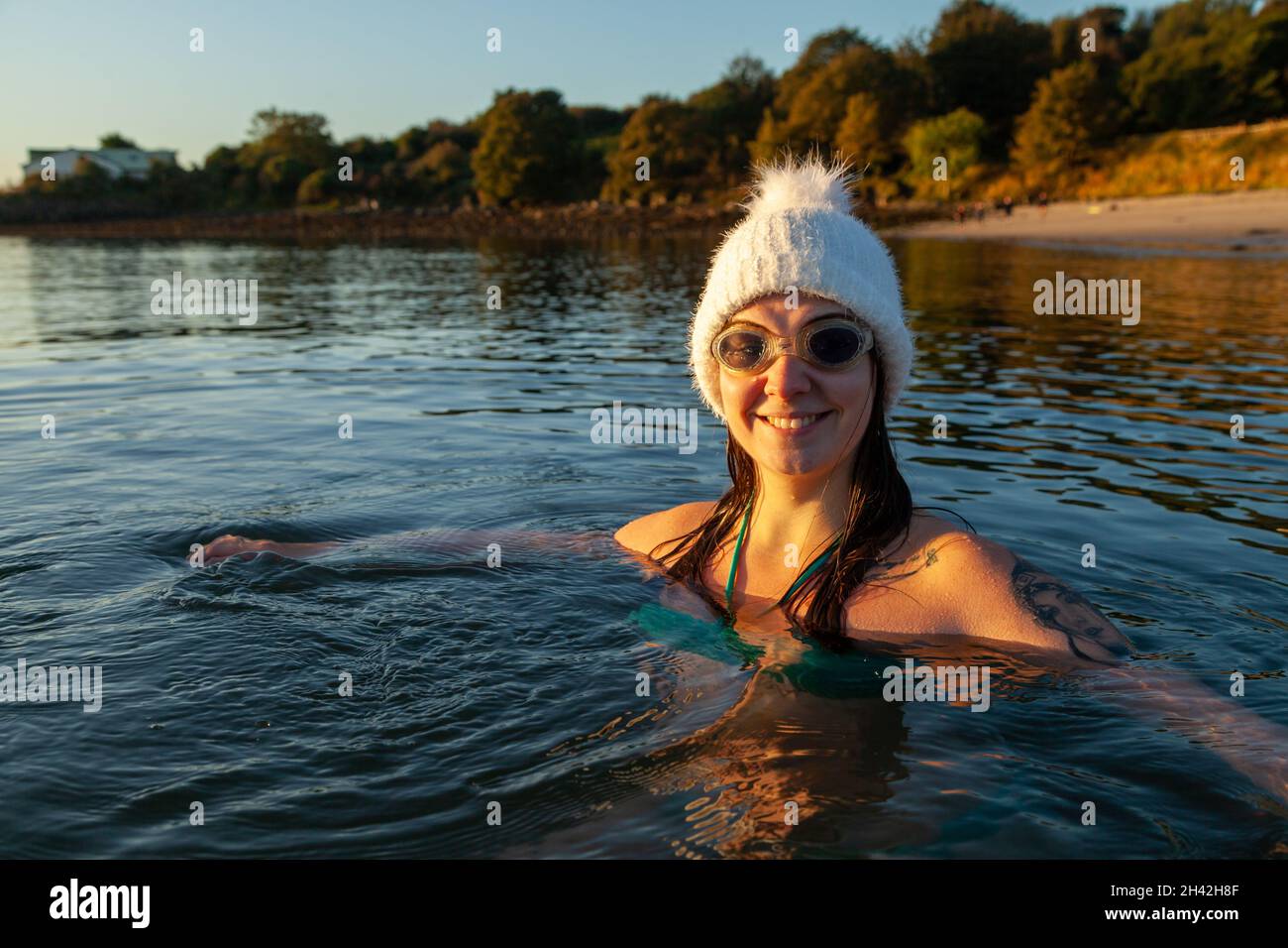 Una joven escocesa con un sombrero de lana blanca y agua fría nadando en el mar en Aberdour en octubre, Fife, Escocia Foto de stock