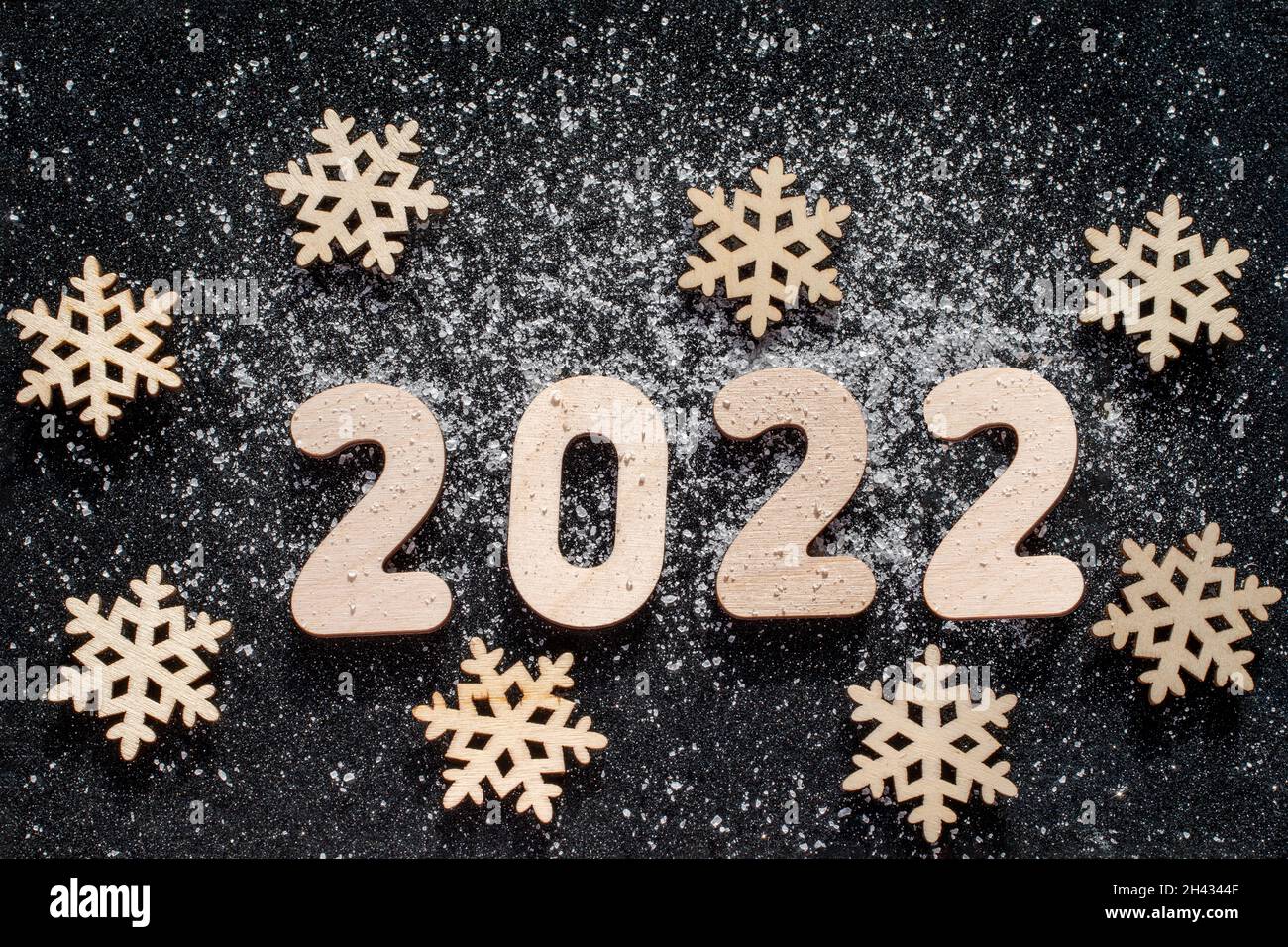 Concepto de Año Nuevo - Snowflakes de madera y números 2022 salpicados de nieve sobre fondo negro brillante de estrellas. Tarjeta Año Nuevo. Foto de stock