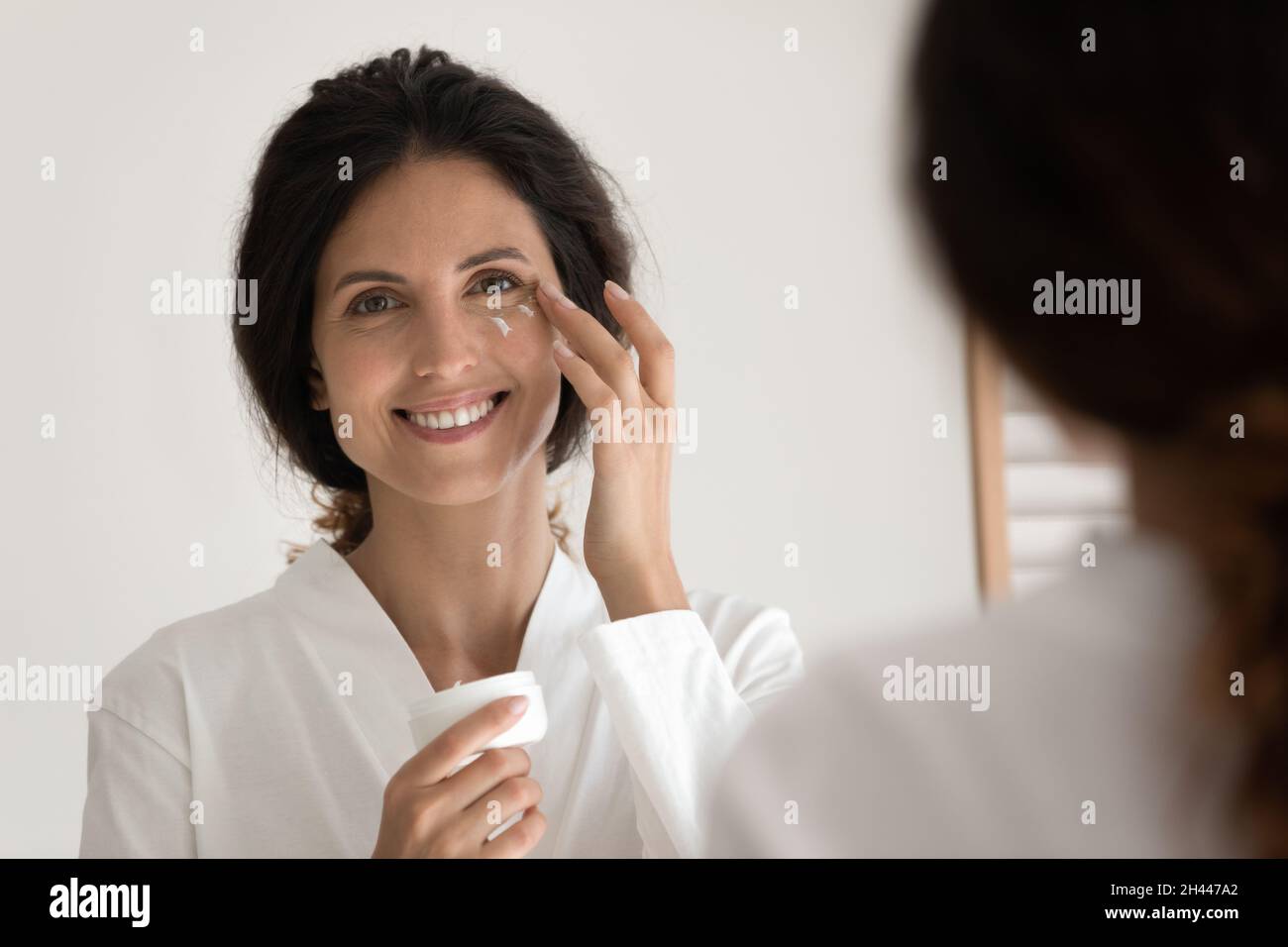 Mujer sostiene el frasco Aplicar crema en las esquinas exteriores de los ojos Foto de stock