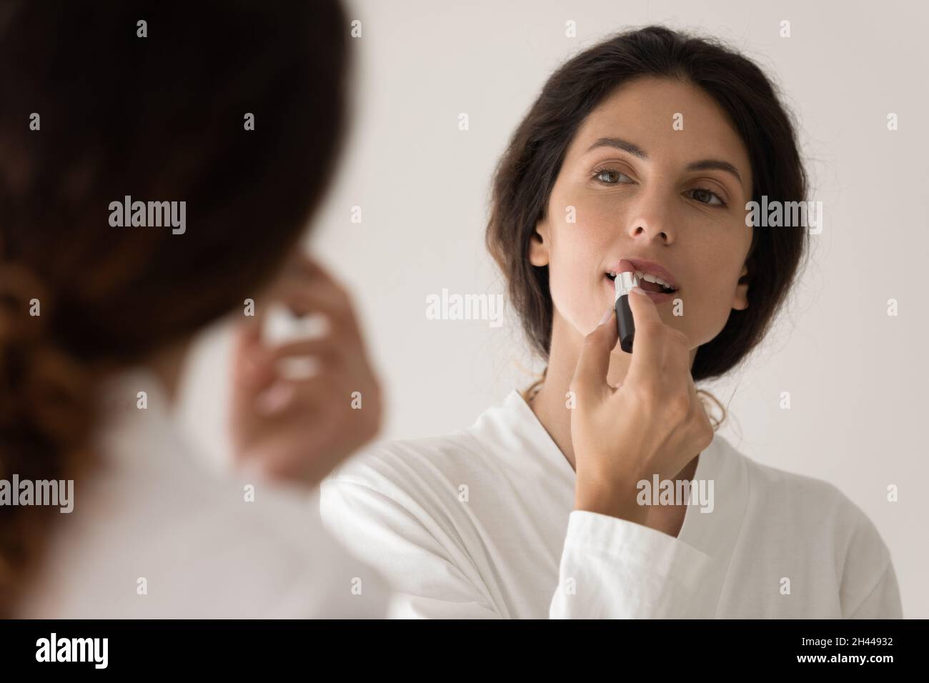 Mujer en el albornoz aplicando lápiz labial en los labios Foto de stock