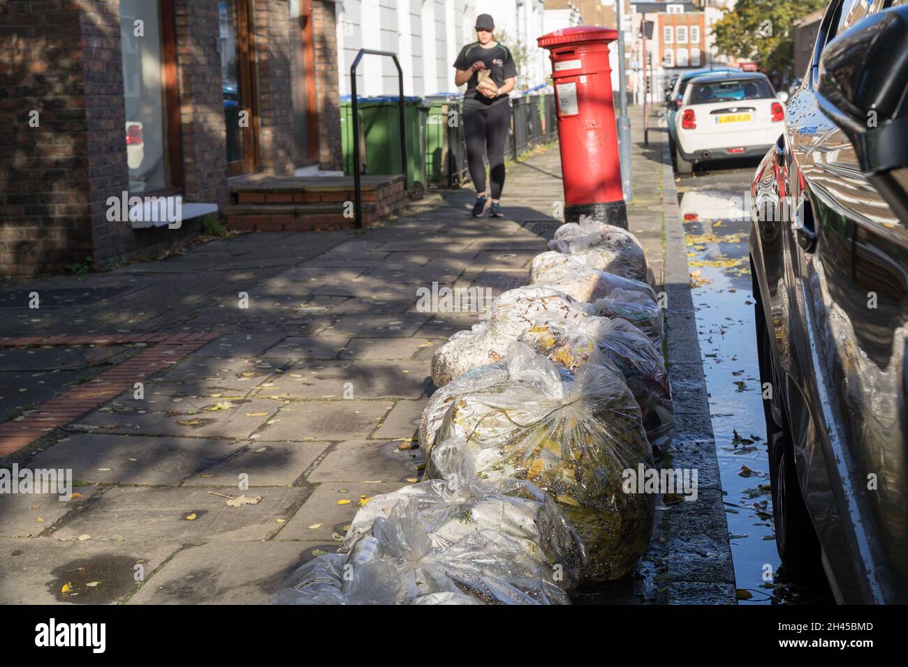 Bolsas de basura y hojas de árboles en el bordillo, pavimento a recoger Londres Greenwich Inglaterra Reino Unido Foto de stock