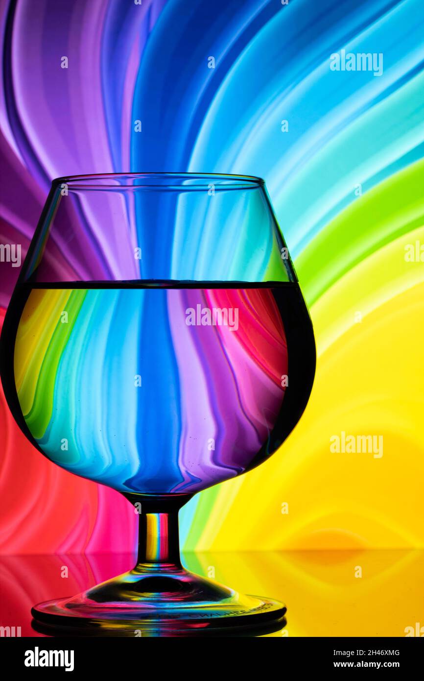 Imagen abstracta de un vidrio coñac sobre un fondo coloreado con curvas y una superficie de espejo Foto de stock