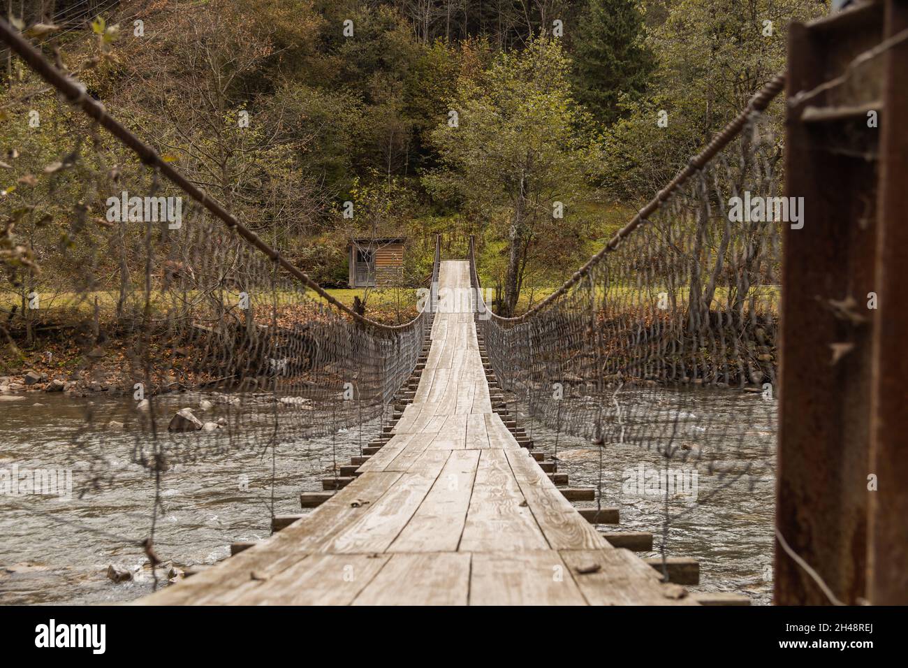 Antiguo puente colgante de madera a través del río de montaña entre el bosque de otoño. Imagen Moody. Fondo del campo. Foto de stock
