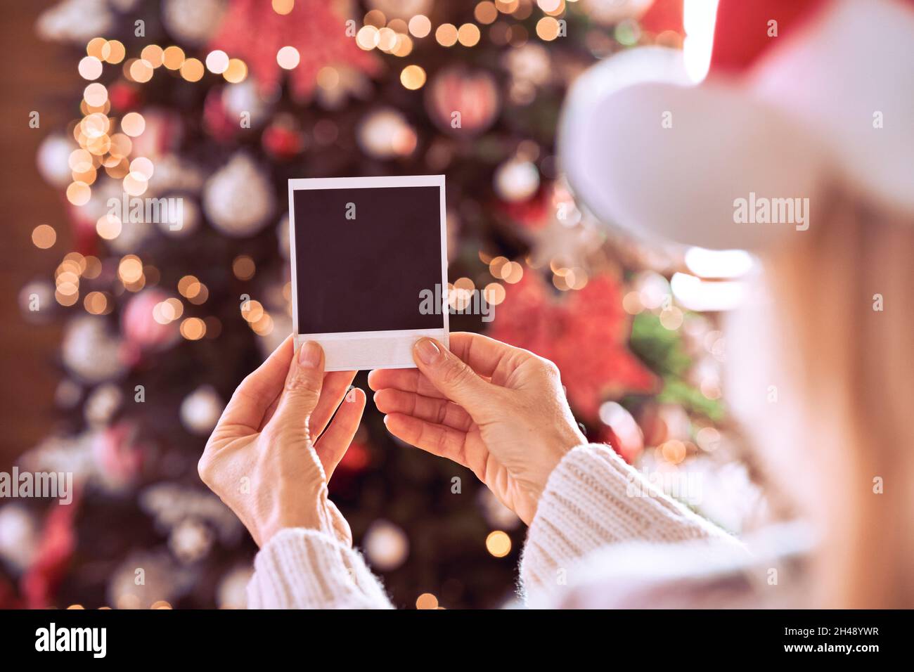 Mujer mano sosteniendo tarjeta de Navidad con regalo en el fondo del árbol de Navidad. Foto de stock