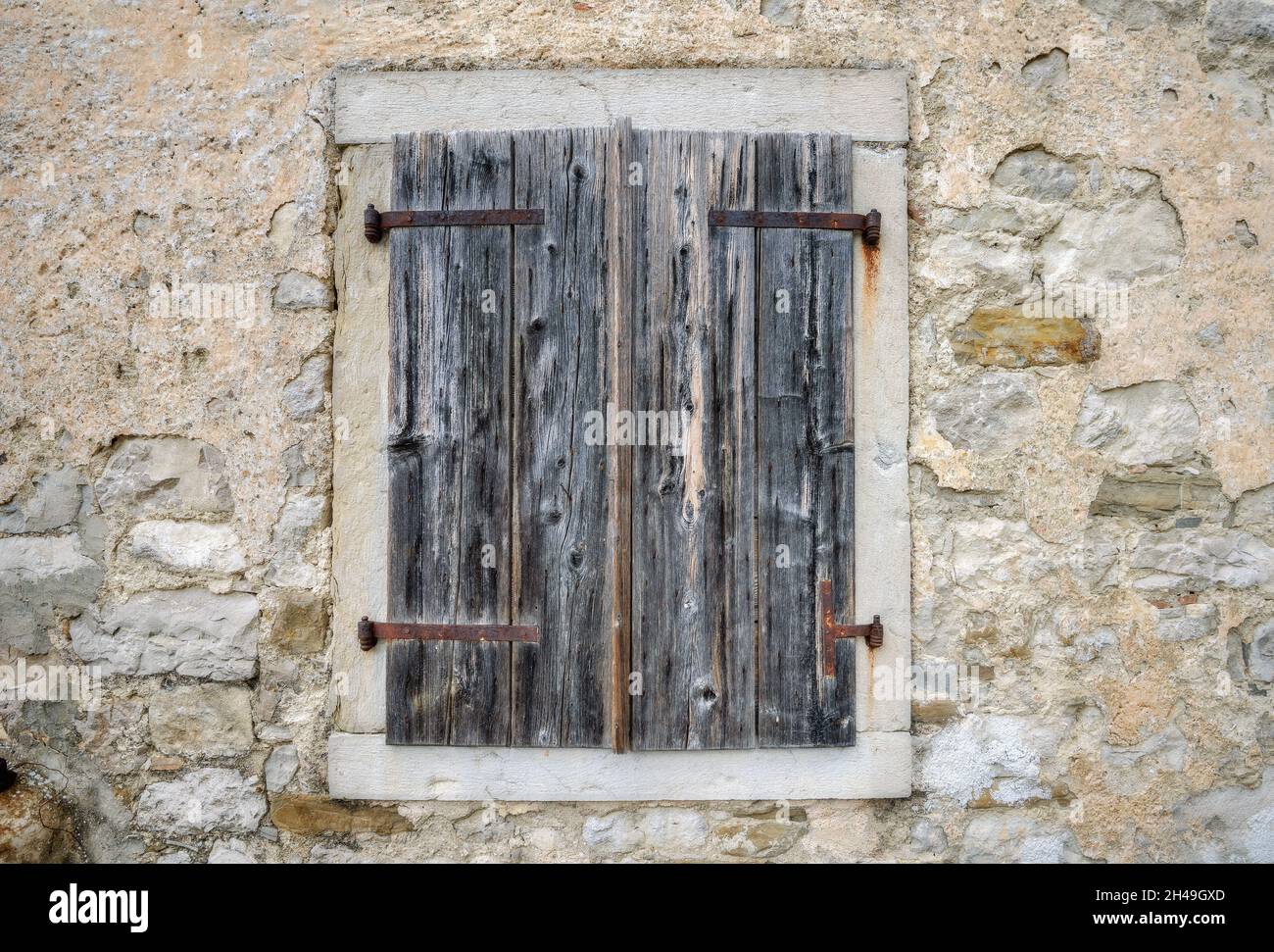Cerca de una ventana con persianas de madera en la pared de piedra de la casa antigua. Hum, Croacia Foto de stock