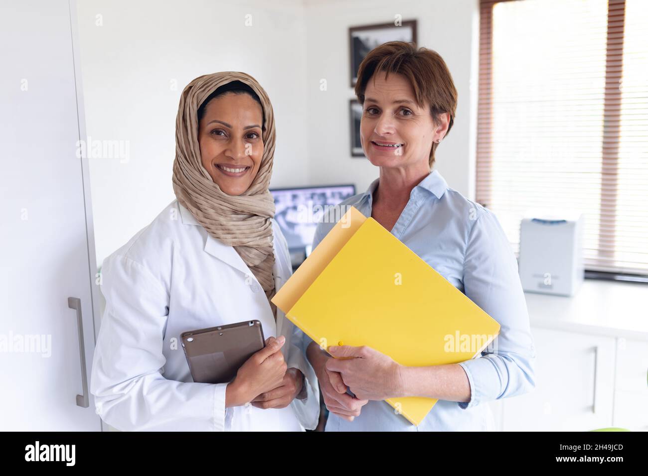 Retrato de una mujer dentista biracial sonriente y enfermera dental femenina en una clínica dental moderna Foto de stock