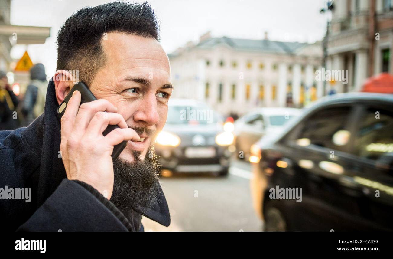 Retrato de un chico hipster que llama a un taxi en el centro de la ciudad - Hombre de moda otoñal en el momento del tráfico urbano - Hombre joven con barba y bigote Foto de stock