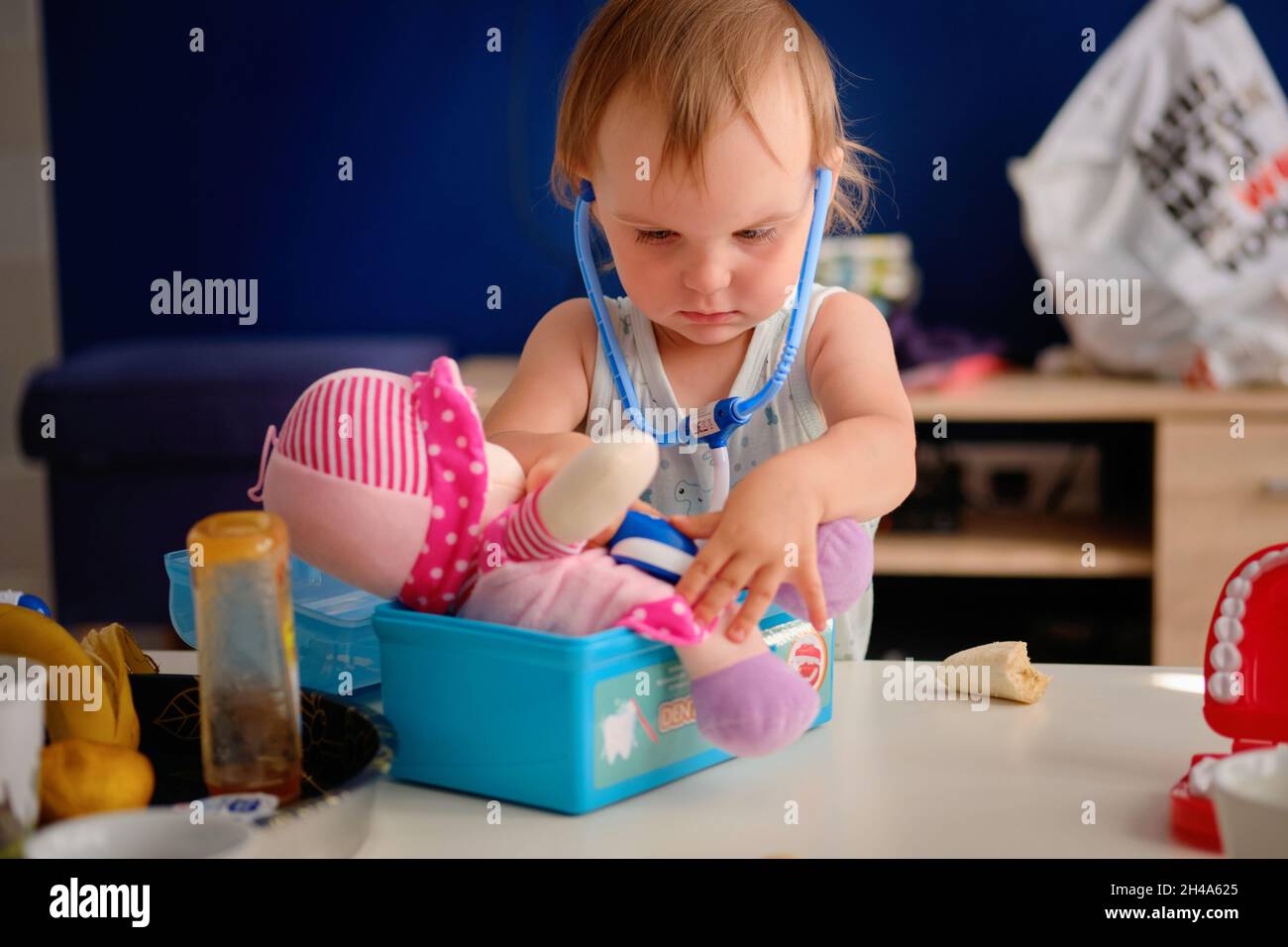 adorable rubia niña juega el papel de un médico jugando con su muñeca de trapo rosa Foto de stock