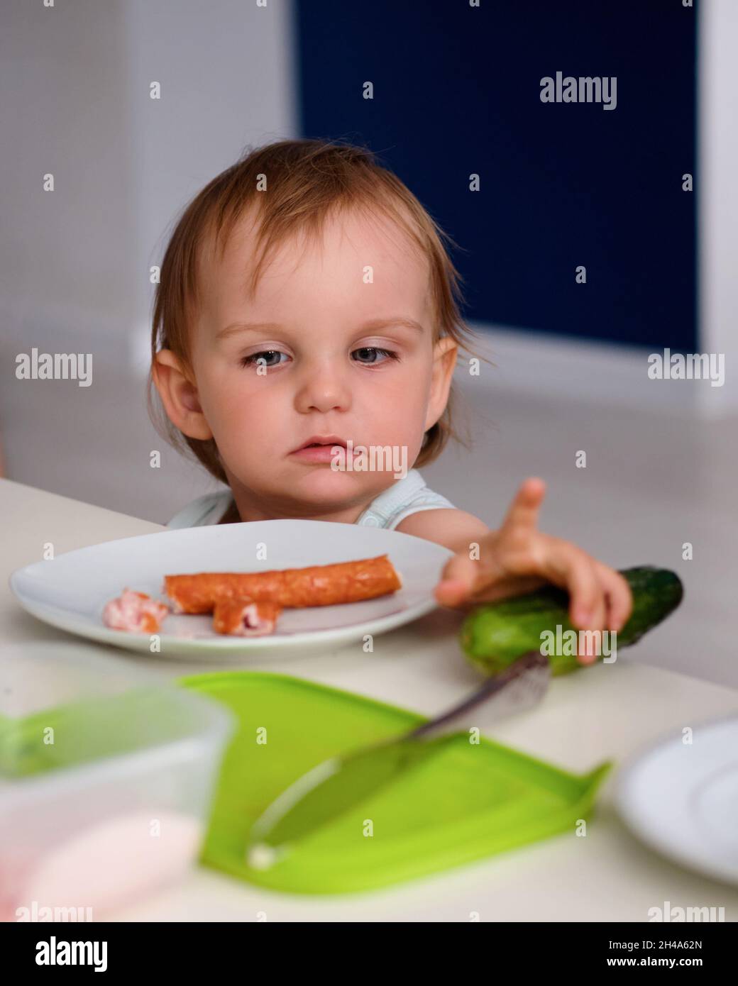 un primer plano de una niña sentada en la mesa mirando una salchicha acostada en un plato Foto de stock