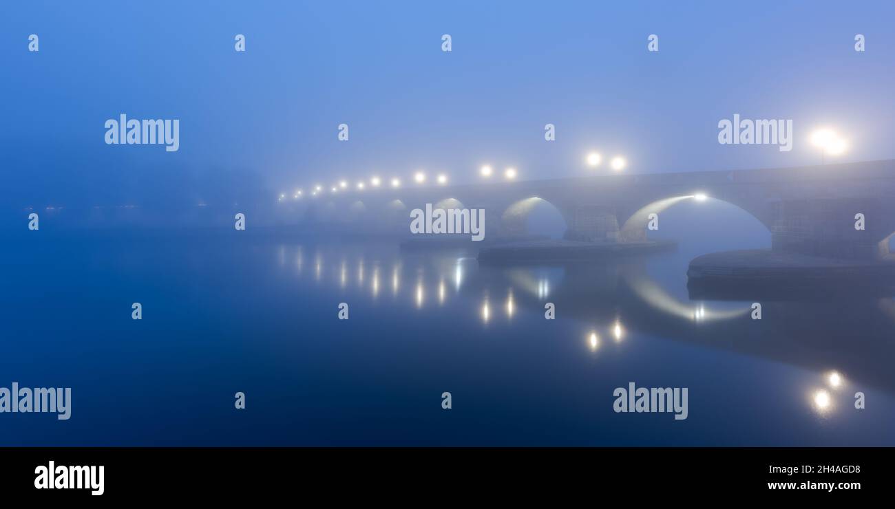 Panorama del famoso puente de piedra sobre el río Danubio en Regensburg, Baviera en una mañana fría al amanecer con niebla y niebla pesadas Foto de stock