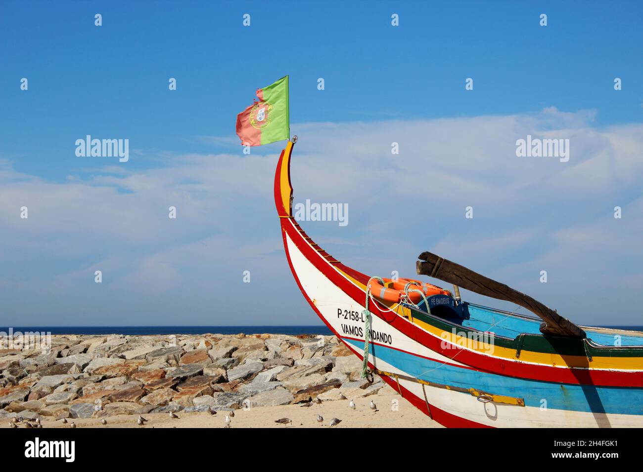 Ein buntes, altes Fischerboot aus Holz und mit rot Grüner Flagge am Strand von Espinho, Portugal. Im Hintergrund Möwen und Meer. Foto de stock