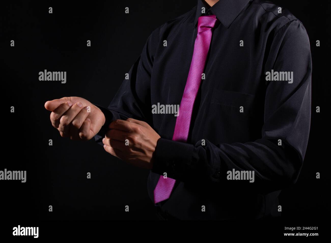 Hombre elegante que fija las mangas de su traje. Camisa negra y corbata  púrpura. Hombre desconocido. Aislado sobre fondo negro Fotografía de stock  - Alamy