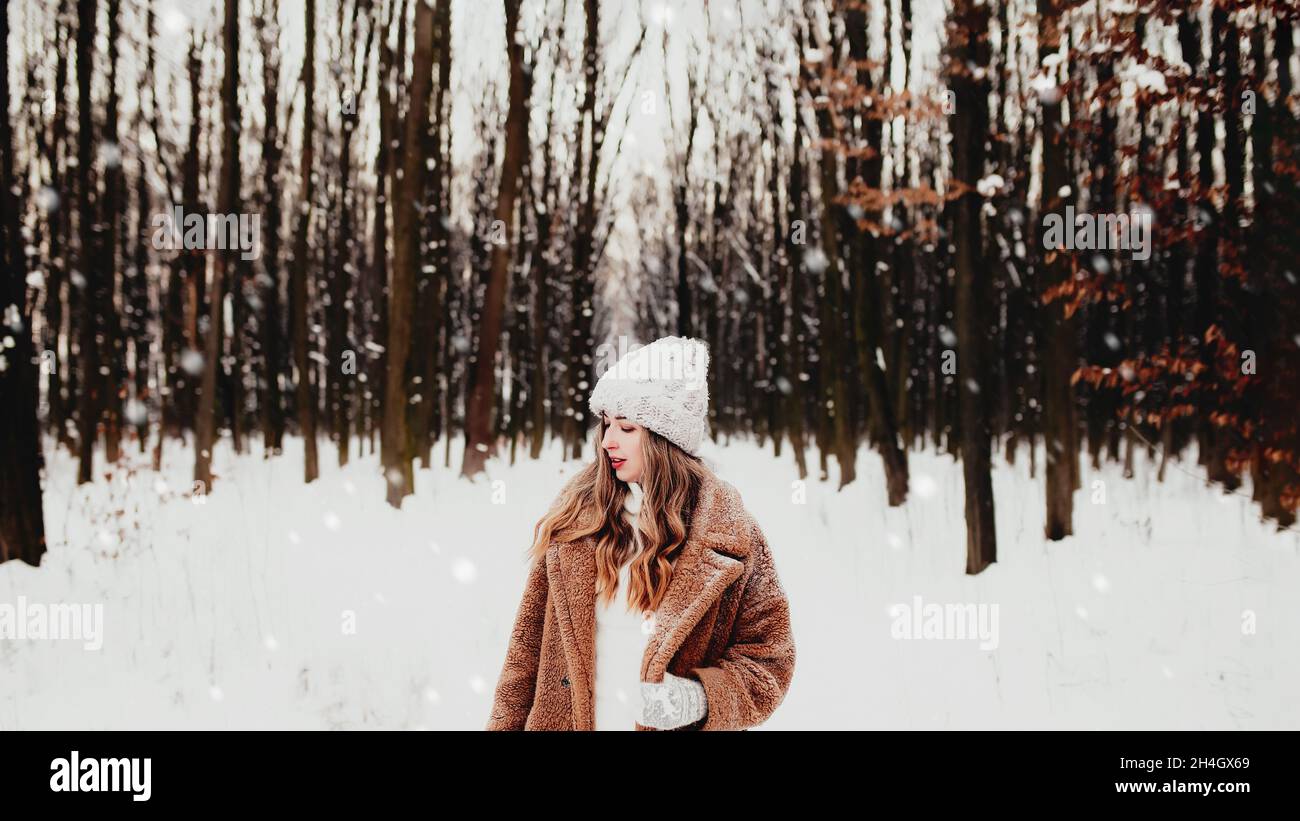 Feliz mujer joven en ropa de invierno de pie en el bosque