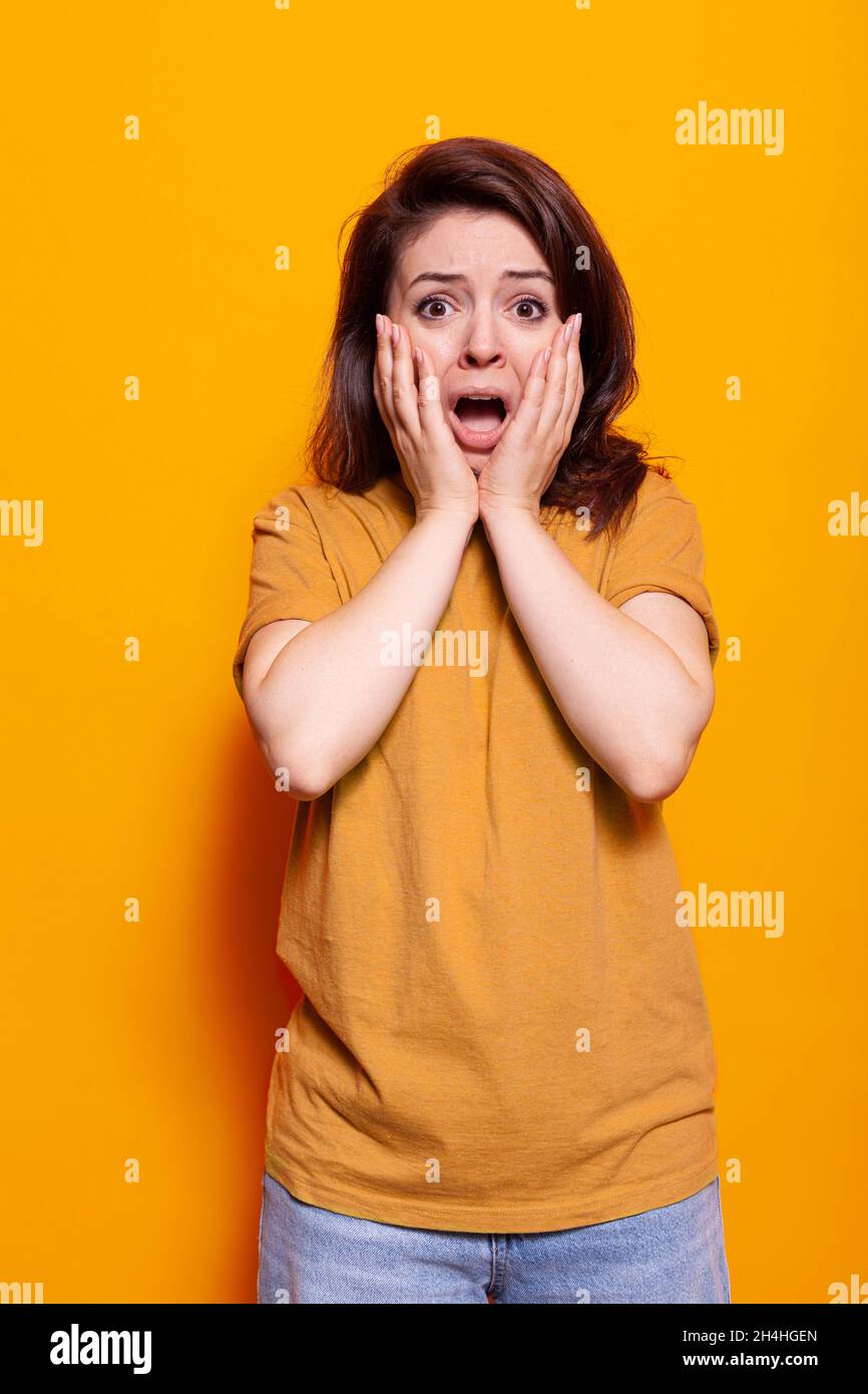 Retrato de una mujer horrorizada con las manos en la cara y la boca abiertas para posarse en la cámara. Mujer gritando y teniendo miedo, teniendo expresión ansiosa en el estudio. Adulto asustado con emociones Foto de stock