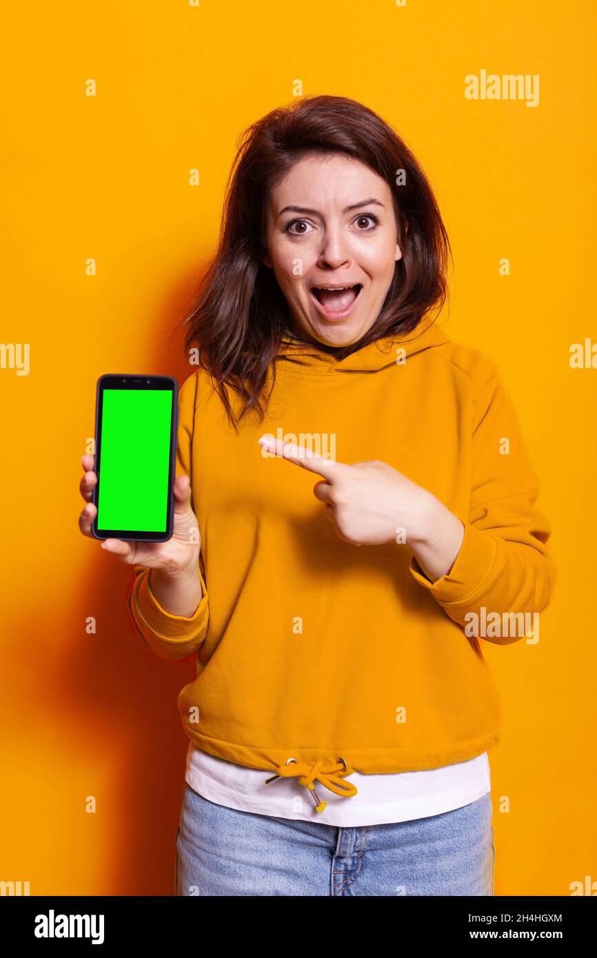 Mujer joven apuntando a la pantalla verde vertical del smartphone