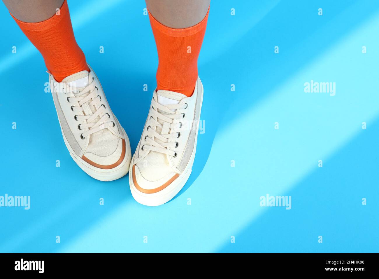Piernas de mujer en calcetines naranjas y sneakers sobre fondo azul Foto de stock