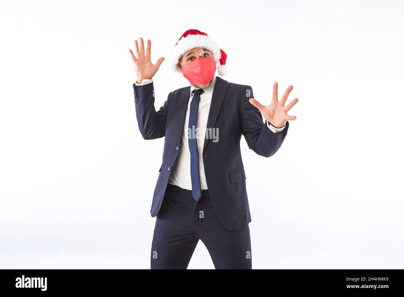 Hombre de negocios vestido con traje, corbata, sombrero de Navidad de Santa  Claus y máscara roja, levantando las manos divirtiéndose, sobre fondo  blanco. Concepto de celebración de Navidad Fotografía de stock -