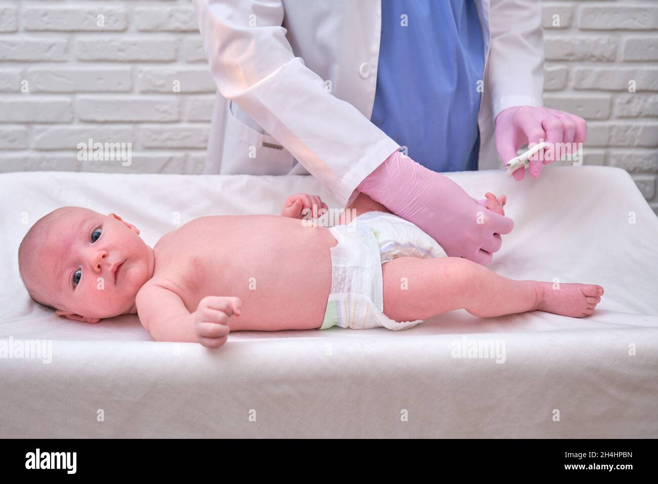 El médico corta las uñas de los pies de un bebé recién nacido. Una  enfermera uniforme con tijeras para la higiene de las piernas y pies del  niño Fotografía de stock 