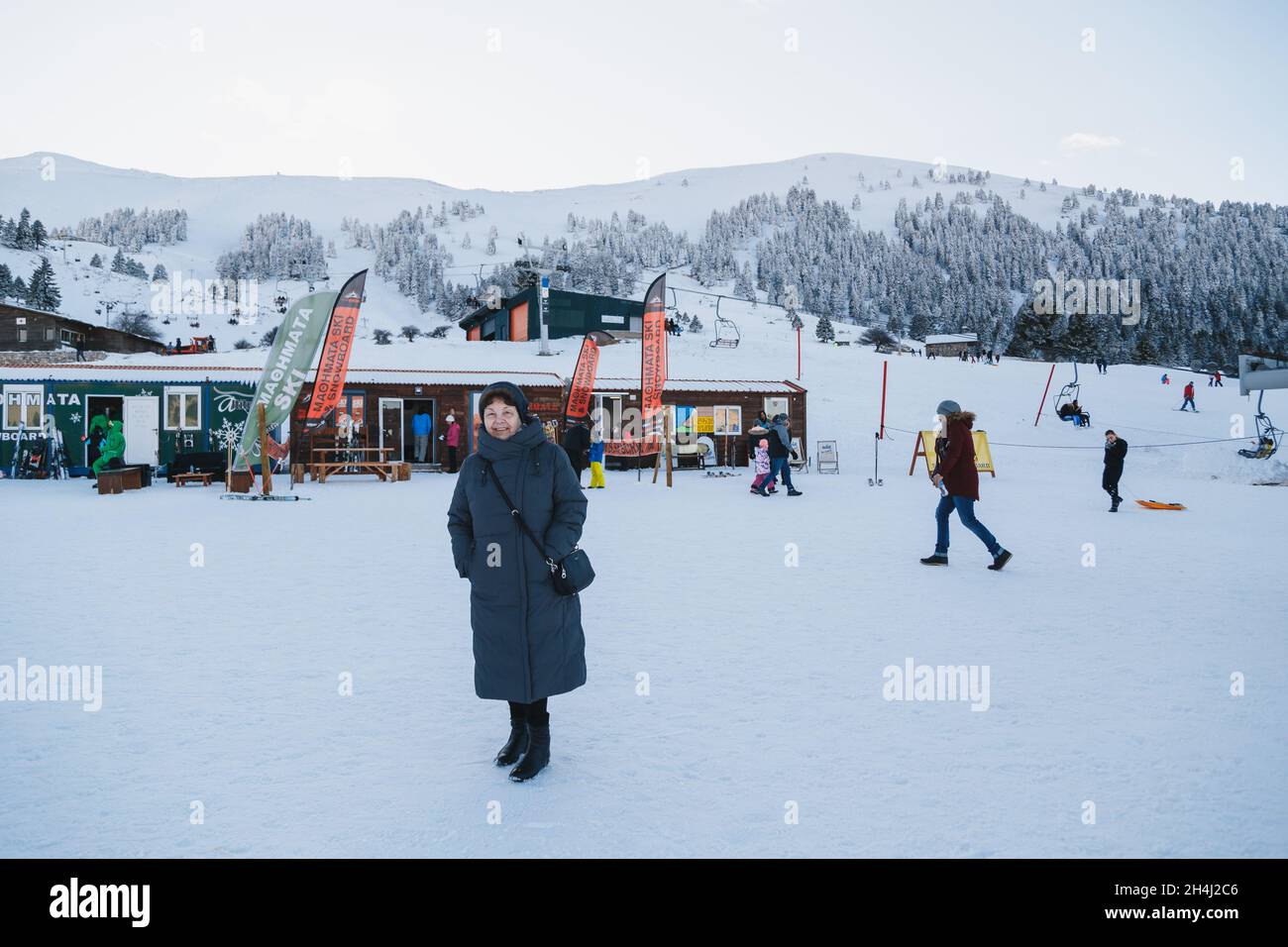 Kalavryta ski Resort, Grecia - enero de 1 2020: Hermosa mujer mayor con abrigo gris en el centro de alquiler de la estación de esquí con vistas a las montañas cubiertas de nieve en el fondo. Vacaciones de invierno Foto de stock