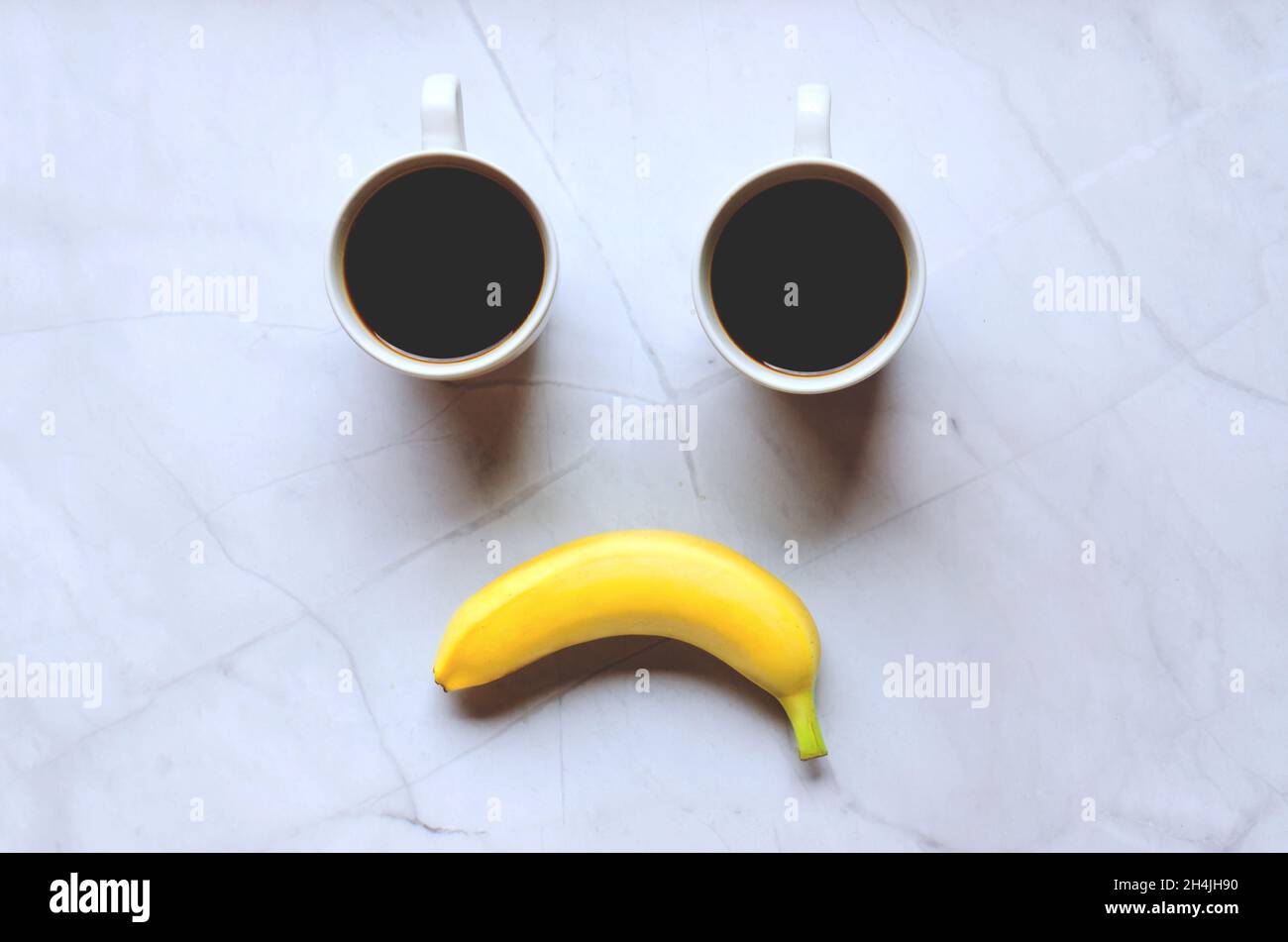 Hombre de negocios trabajando por la mañana con tazas de café negro caliente y plátano amarillo sobre fondo blanco. Vista superior, espacio de copia, maqueta. Capa plana. Emoción feliz Foto de stock