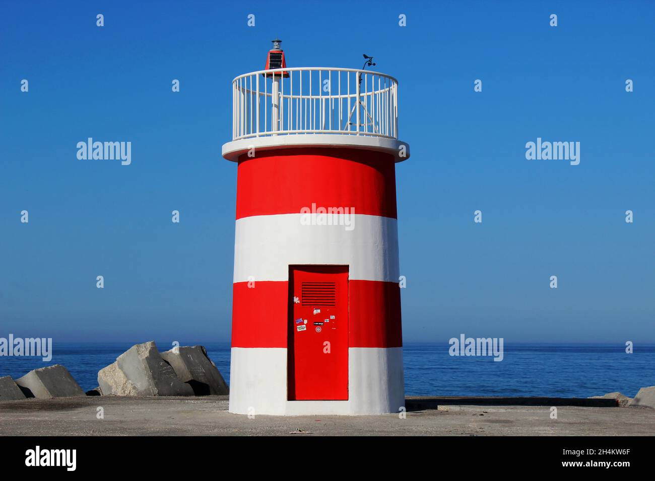 Der rot weiß gestreifte Leuchtturm auf dem nördlichen Steg am Strand von Nazare, Portugal. Portugiesische Bezeichnung: Farol Nazaré Pontão Norte. Foto de stock