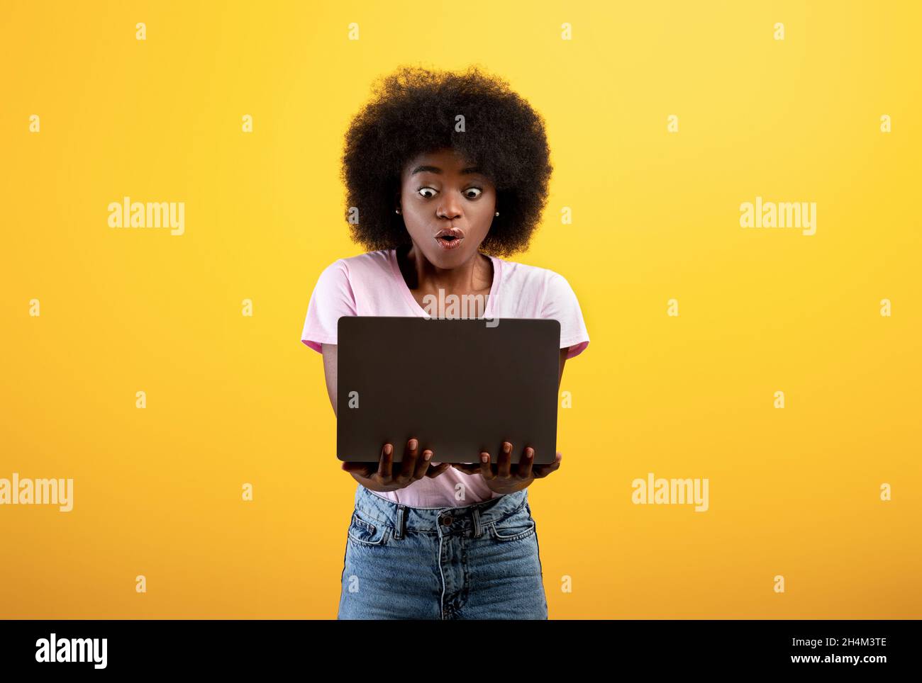 Contenido de choque. Dama negra abrumada mirando la pantalla del ordenador portátil, sosteniendo el ordenador de la pc, recibiendo noticias o sufriendo de estafa del Internet, de pie en yello Foto de stock