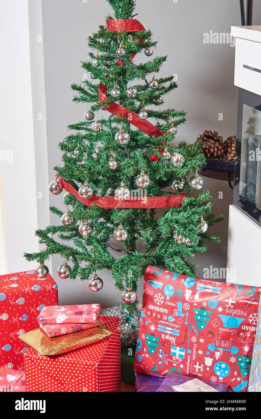 Regalos de Navidad envueltos con papel de colores bajo el árbol de Navidad  decorado con bolas y cinta roja Fotografía de stock - Alamy