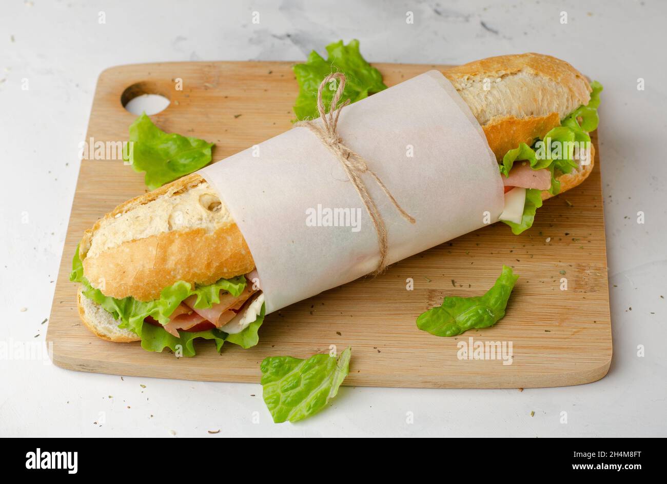 Sub delicatessen bocadillo baguette con jamón, queso, tomates y lechuga vista superior en tabla de cortar Foto de stock