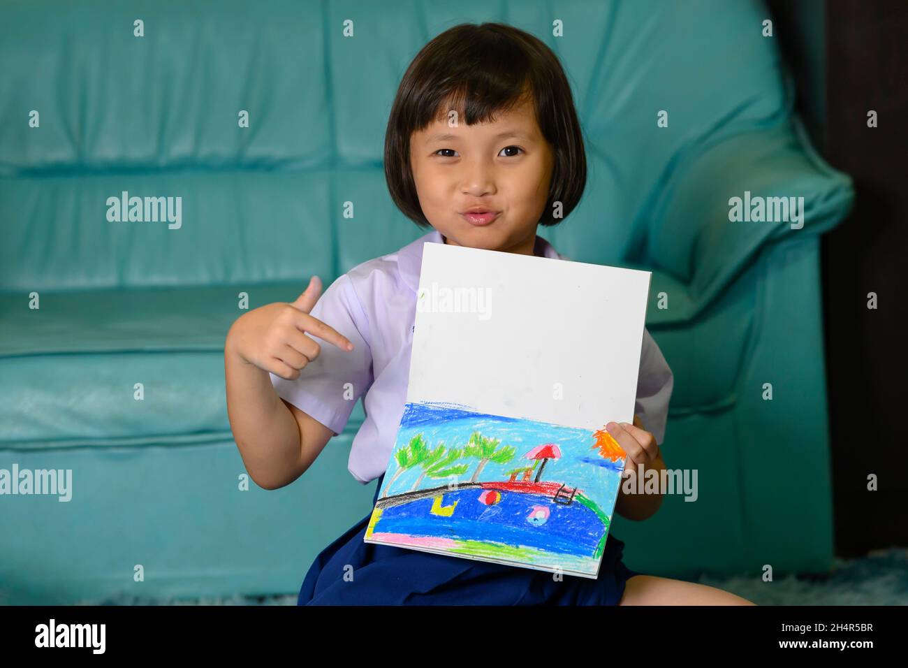 pequeña niña escribiendo y coloreando con tiza crayón mientras se relaja en la alfombra en casa después de volver de la escuela Foto de stock