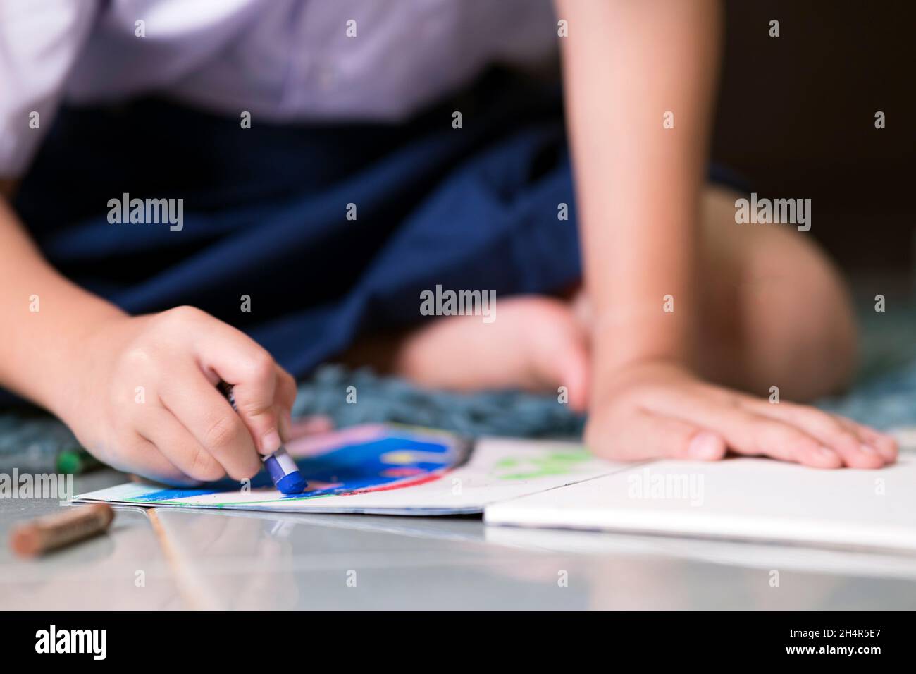 pequeña niña escribiendo y coloreando con tiza crayón mientras se relaja en la alfombra en casa después de volver de la escuela Foto de stock