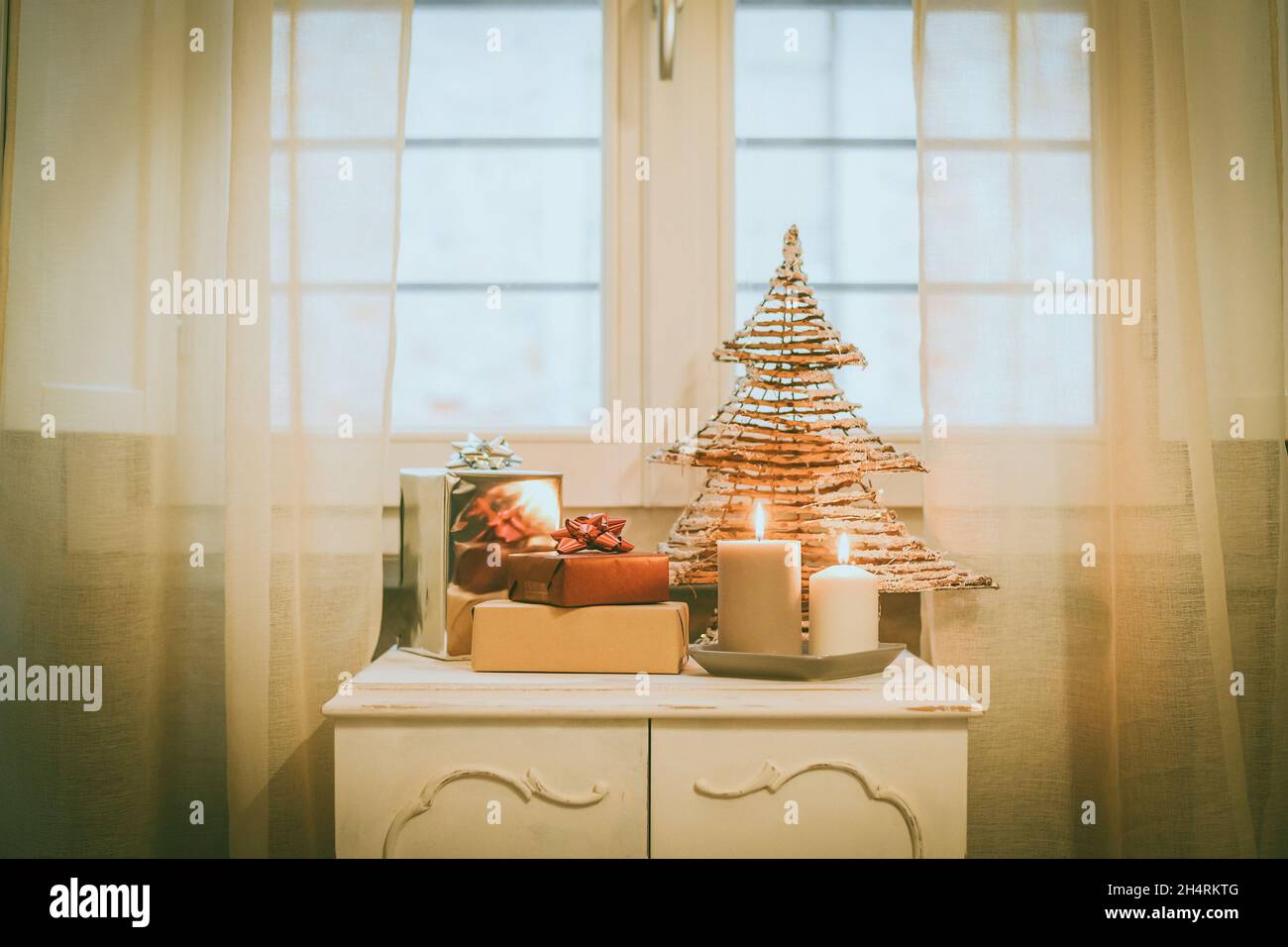 Cajas de regalo cerca de velas encendidas y árbol de Navidad dentro de la  casa. Caja con cinta de vacaciones con ventana de arcos en el fondo. Cálido  ambiente festivo familiar Fotografía