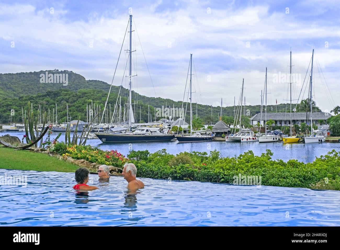 Barcos de vela y yates amarrados en English Harbour y turistas occidentales en la piscina de la isla Antigua, Antillas Menores en el Mar Caribe Foto de stock