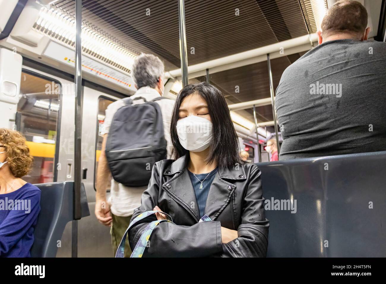 Barcelona, España - 21 de septiembre de 2021: Mujer asiática exhausta tomar una siesta en el tren durante su camino a casa, usando máscara protectora de la cara debido a cor Foto de stock