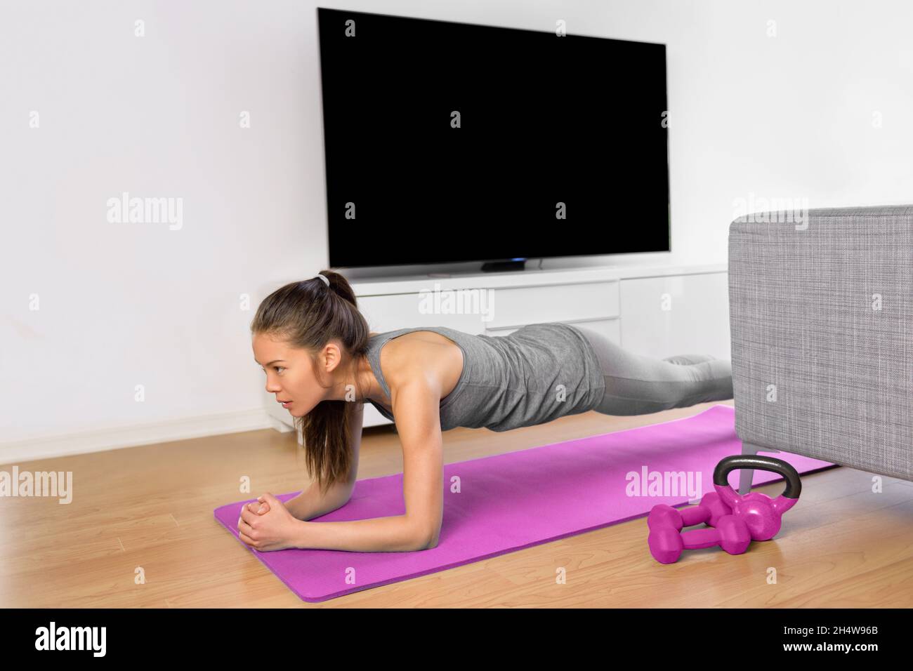Sala de estar de ejercicio de fitness - chica haciendo ejercicios de tabla  para hacer ejercicio de la base en casa. Mujer asiática joven entrenando  músculos delante de la TV como parte