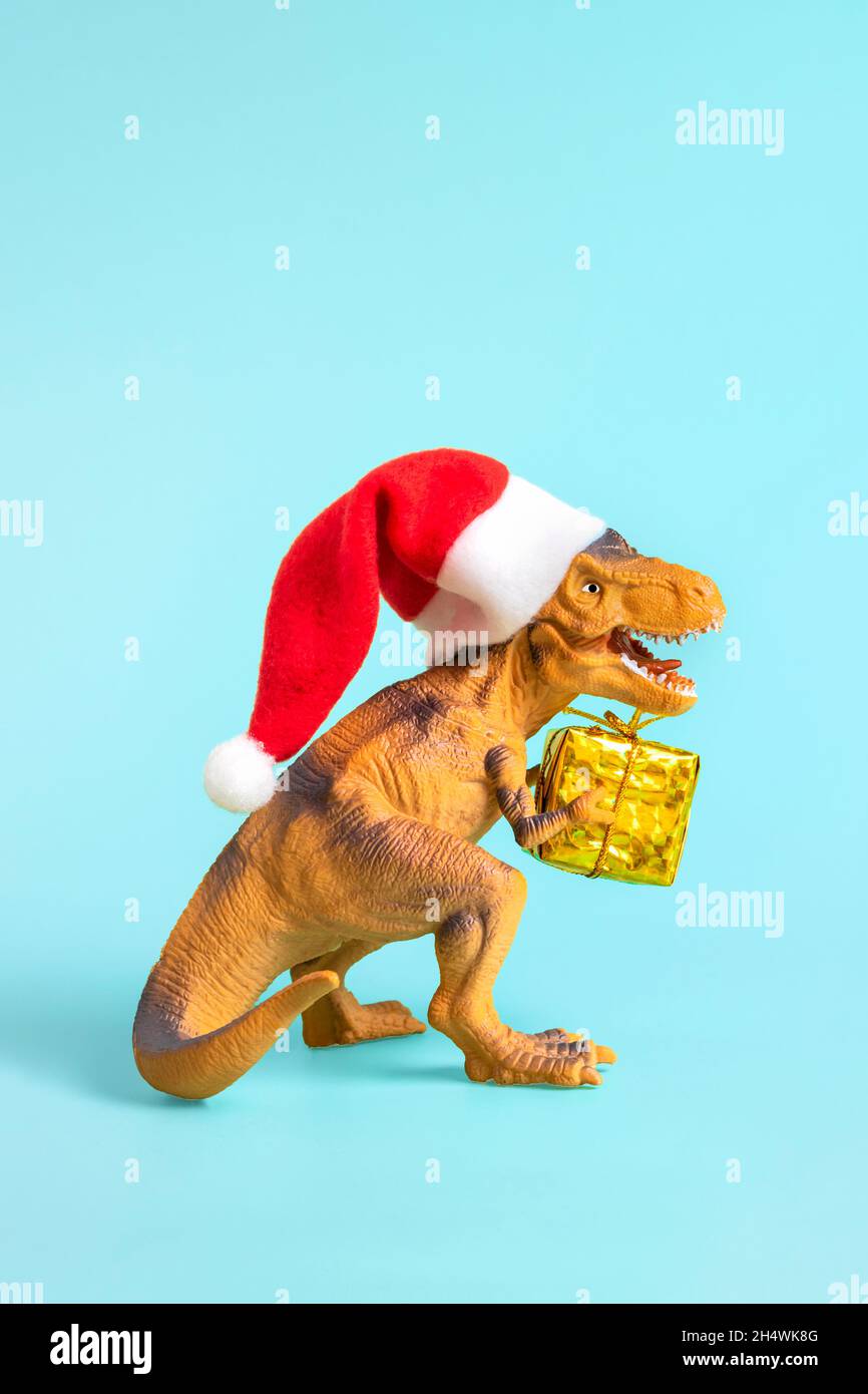 Dinosaurio Rex en rojo Santa Claus sombrero sostiene caja de regalo de oro  en sus patas sobre fondo azul de Nochevieja o de Nochebuena Arte tarjeta de  vacaciones idea creativa Fotografía de