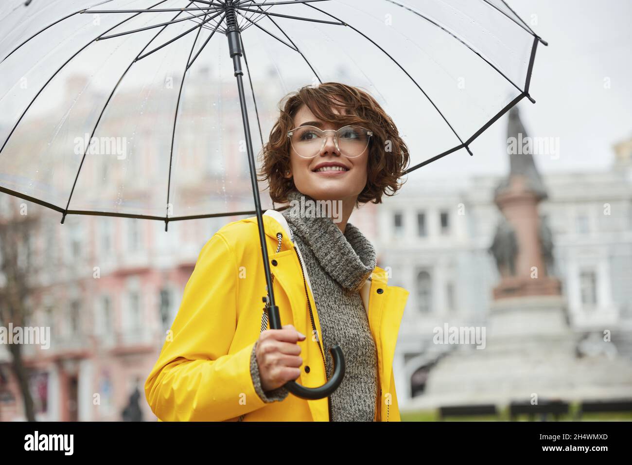 Chica joven con chubasquero amarillo con paraguas transparente en