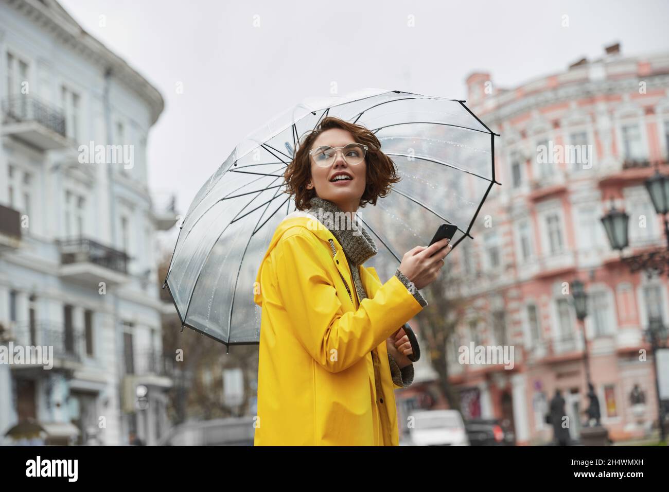 Chica caucásica en chubasquero amarillo con transparente en la ciudad. Joven hermosa mujer con traje de lluvia mientras camina en calle durante el día. Con Fotografía de stock - Alamy