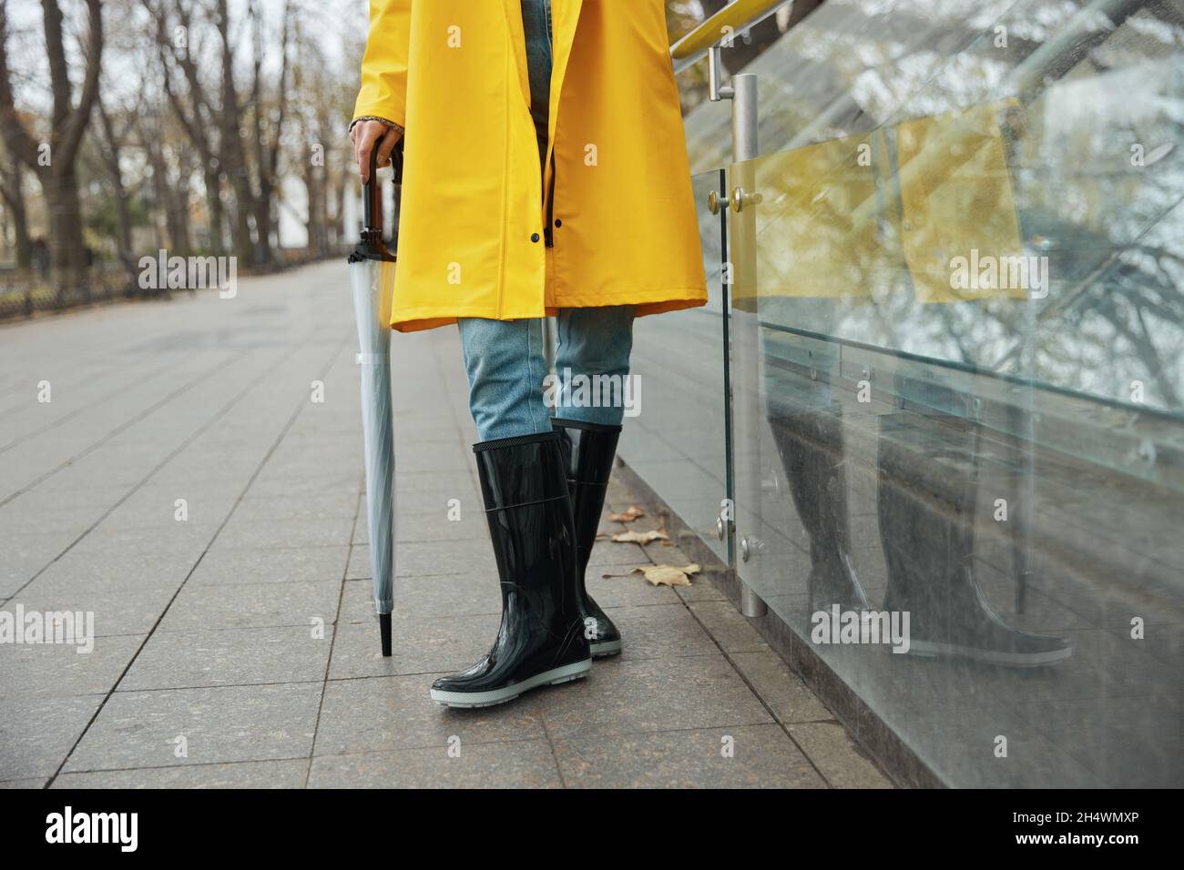 Chica con chubasquero amarillo y chubasquero con paraguas transparente en la ciudad. Mujer joven que lleva traje de lluvia galoses mientras en la calle. Concepto stock - Alamy