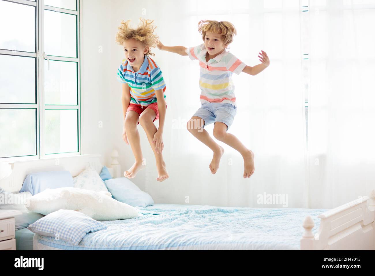 comentario Cliente codo Un niño saltando en la cama en un dormitorio blanco con una ventana grande.  Los niños juegan en casa. Divertido salto en la cama de los padres.  Habitación y diseño interior. Niño